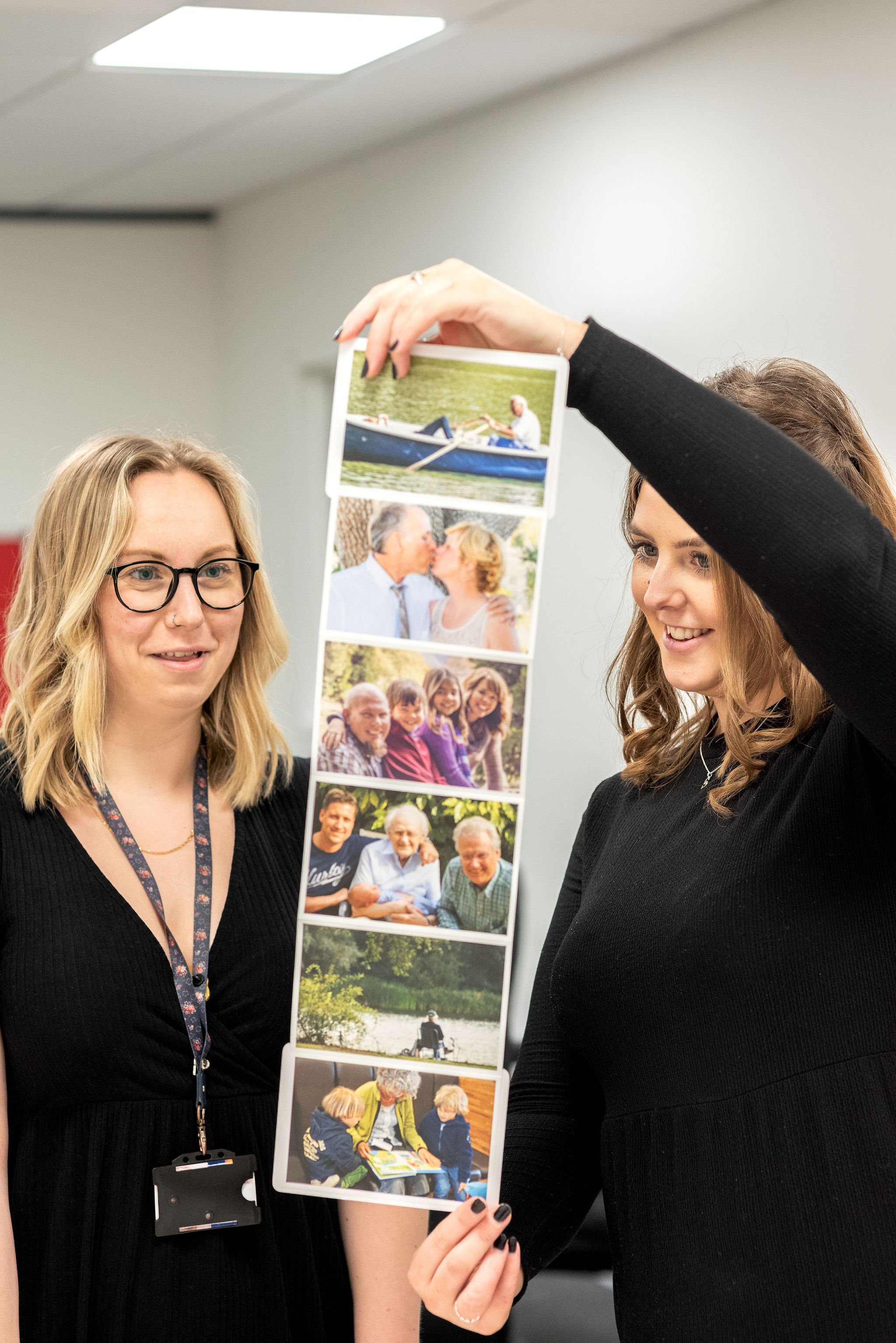 Two women holding a photo strip with six outdoor and family photos, smiling and engaging in conversation.