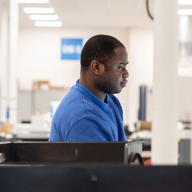 A man wearing a blue shirt working at a computer in an office setting, focused on the screen.