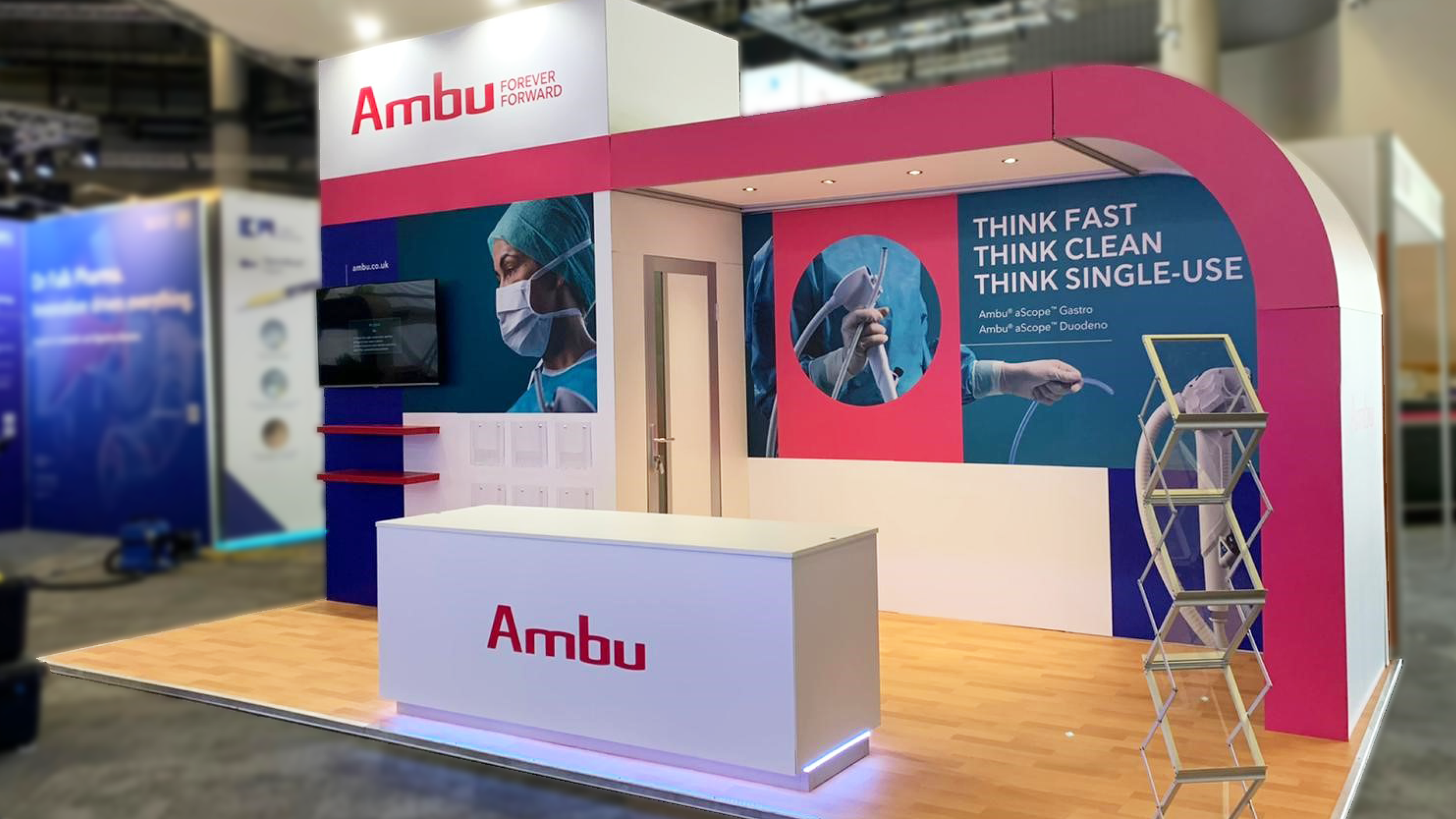Trade show booth for Ambu with pink and blue color scheme featuring medical images and text that says "Think Fast, Think Clean, Think Single-Use".