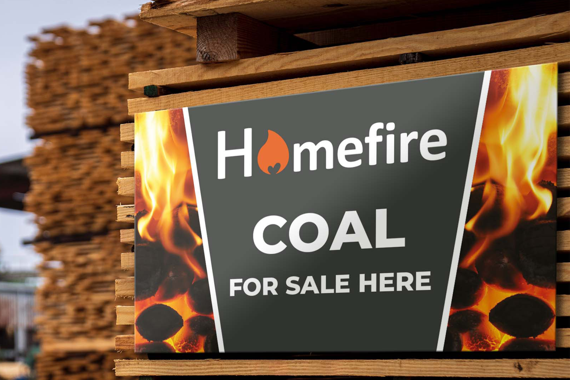 Sign advertising Homefire coal for sale, with flames and burning coal images on its sides, placed against a stack of wood logs.